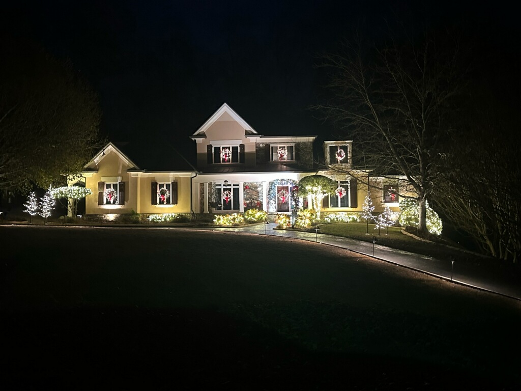 Grand home with Christmas wreaths and window lighting, showcasing extensive holiday light installation along the roof and landscape.