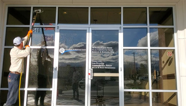 Professional window cleaner using an extension pole to wash large glass storefront windows of a commercial building.